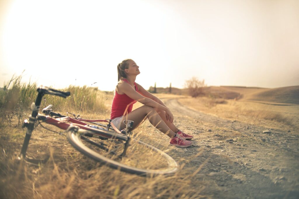 sportive woman with bicycle resting on countryside road in sunlight